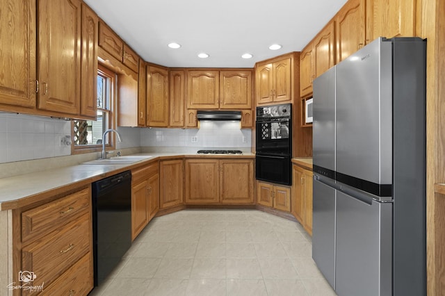 kitchen with black appliances, a sink, under cabinet range hood, brown cabinets, and recessed lighting