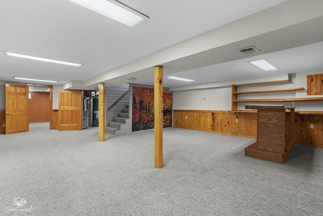 finished basement with stairs, wooden walls, light carpet, and wainscoting