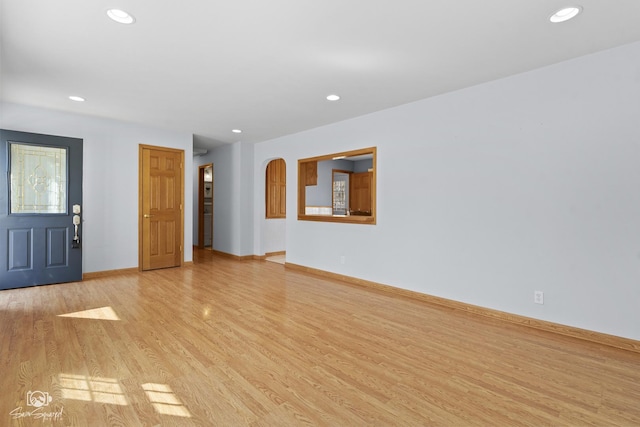 unfurnished living room featuring light wood-style flooring, recessed lighting, baseboards, and arched walkways