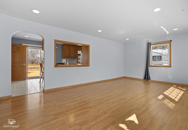 empty room featuring light wood-style floors, arched walkways, recessed lighting, and baseboards
