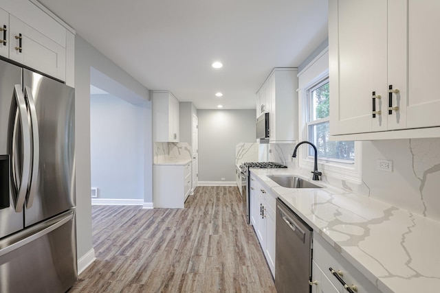 kitchen with stainless steel appliances, a sink, decorative backsplash, light wood-style floors, and light stone counters