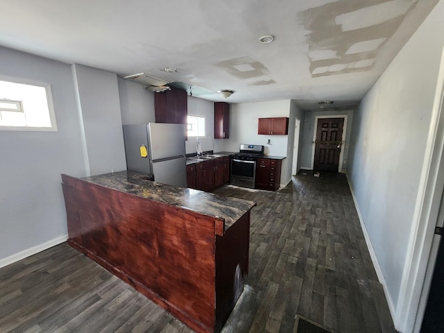 kitchen with appliances with stainless steel finishes, a peninsula, dark wood-style flooring, a sink, and baseboards