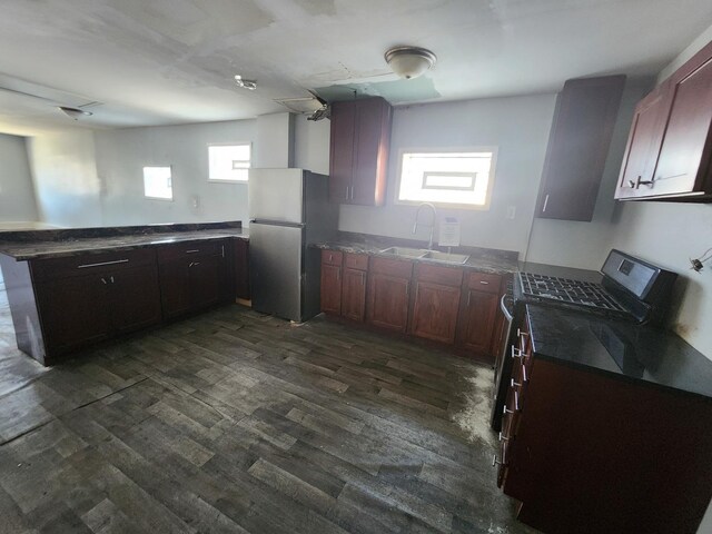 kitchen featuring appliances with stainless steel finishes, a sink, a peninsula, dark wood-style flooring, and dark stone counters