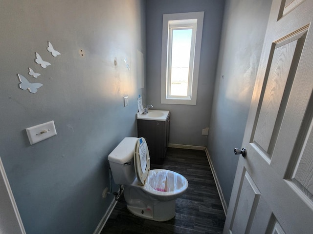 half bath with wood finished floors, baseboards, toilet, and vanity