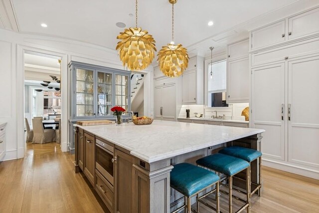 1855 N Hermitage Ave, Chicago, IL 60622 - kitchen with a kitchen island, a decorative wall, light wood-style flooring, a kitchen breakfast bar, and light stone counters