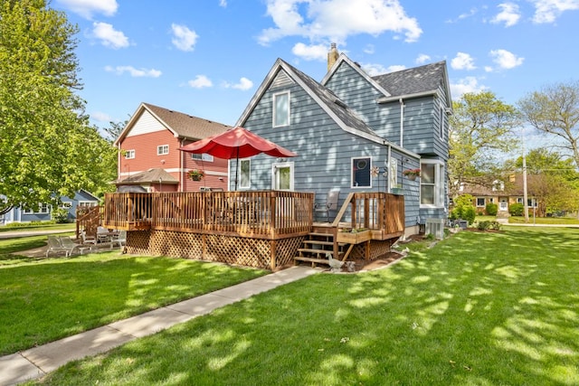rear view of property featuring a chimney, a lawn, a wooden deck, and roof with shingles