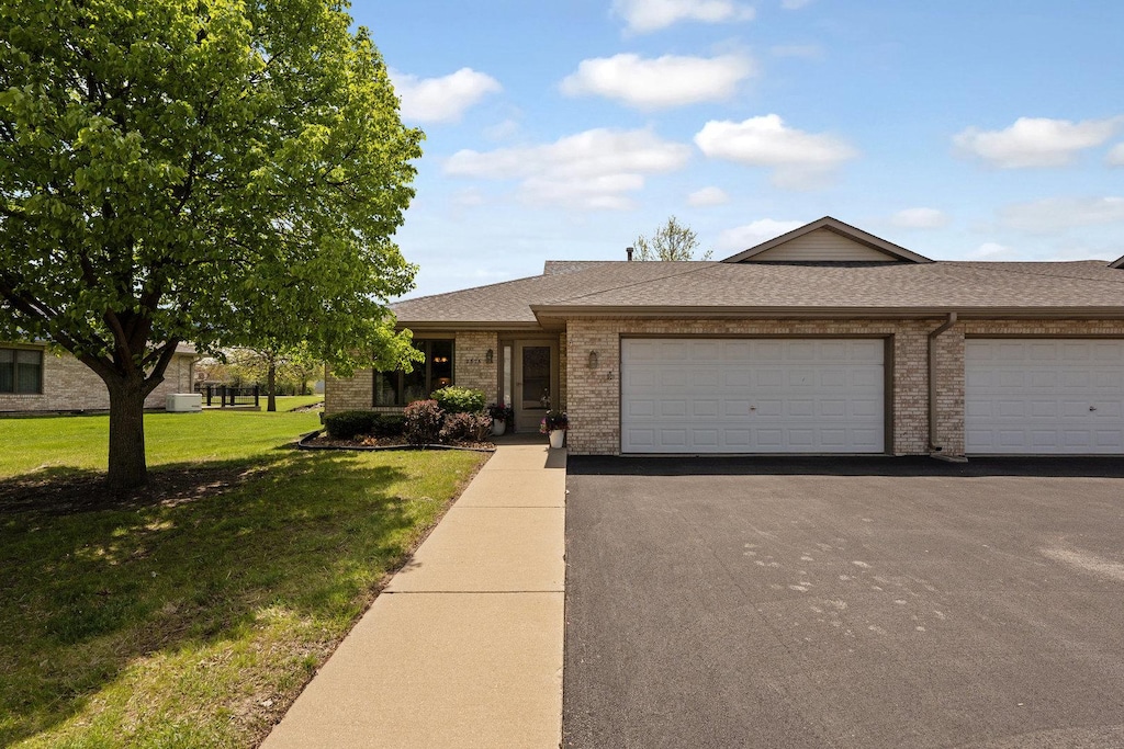 view of front of house with asphalt driveway, an attached garage, brick siding, a front yard, and roof with shingles