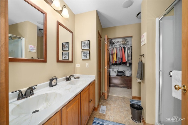 full bathroom with a shower stall, stone finish floors, a walk in closet, and double vanity