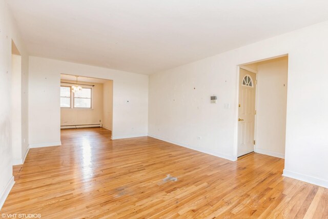 empty room featuring a baseboard heating unit, a chandelier, light wood-style floors, and baseboards