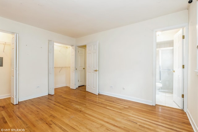 unfurnished bedroom with light wood finished floors, baseboards, connected bathroom, and two closets