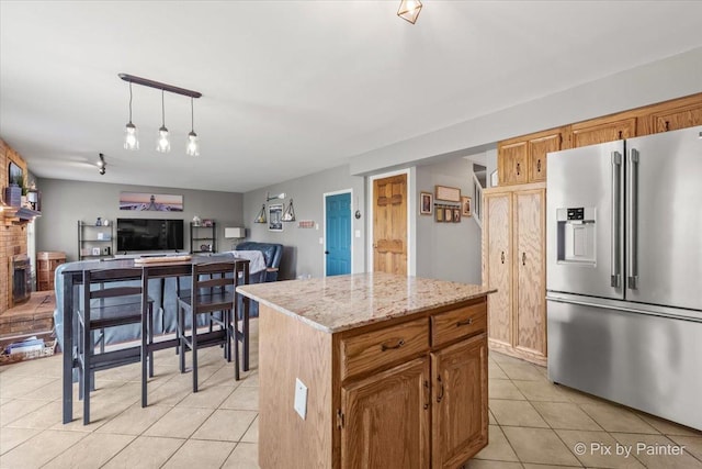 kitchen with high end refrigerator, light tile patterned floors, a kitchen island, light stone countertops, and pendant lighting