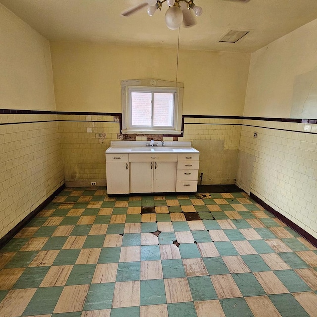 clothes washing area featuring a ceiling fan, a sink, tile walls, wainscoting, and tile patterned floors