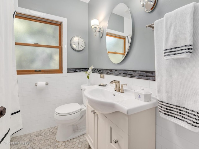 bathroom featuring tile walls, toilet, vanity, tile patterned flooring, and wainscoting