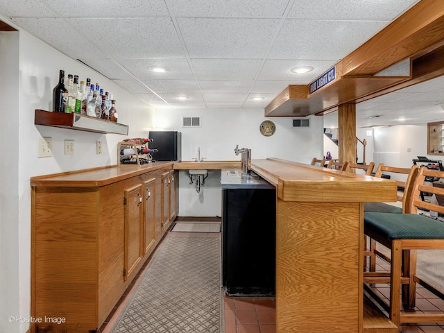 indoor wet bar with a paneled ceiling, recessed lighting, and light tile patterned floors