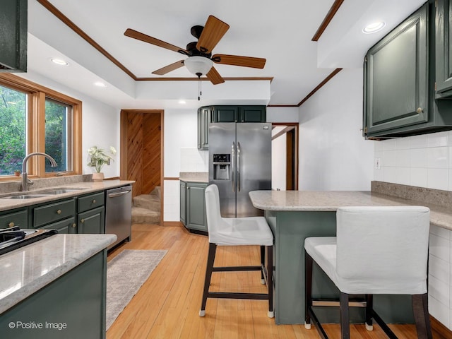 kitchen with appliances with stainless steel finishes, green cabinets, a sink, ornamental molding, and backsplash