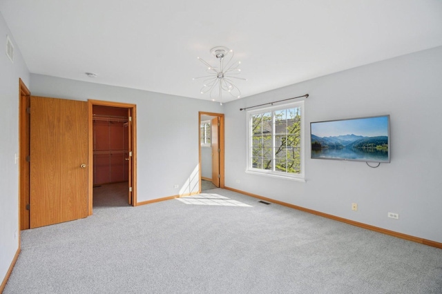 unfurnished bedroom with a chandelier, baseboards, carpet, a walk in closet, and a closet