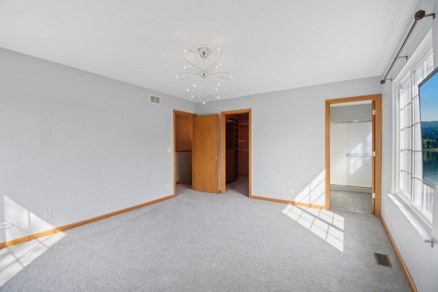 unfurnished bedroom with baseboards, a chandelier, light carpet, a spacious closet, and ensuite bathroom
