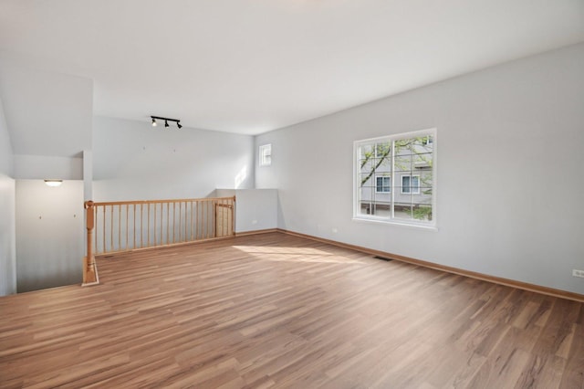 empty room featuring wood finished floors, baseboards, and rail lighting