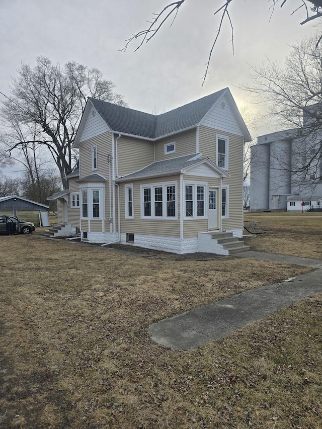 rear view of property with entry steps, a yard, and roof with shingles