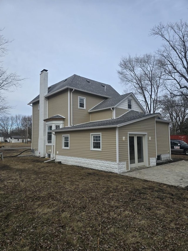 back of property with a chimney, roof with shingles, entry steps, and a patio area