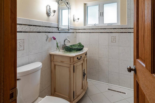 bathroom featuring toilet, vanity, tile walls, tile patterned floors, and wainscoting