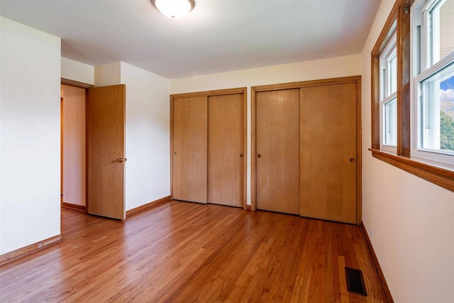 unfurnished bedroom with two closets, light wood-style flooring, and baseboards