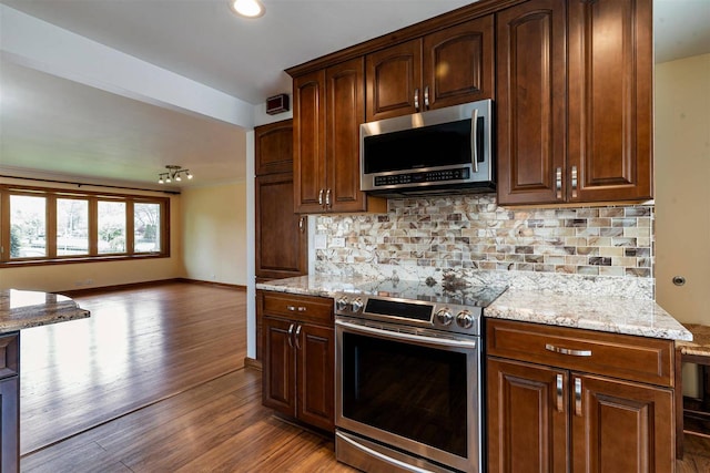 kitchen with appliances with stainless steel finishes, wood finished floors, light stone counters, open floor plan, and tasteful backsplash
