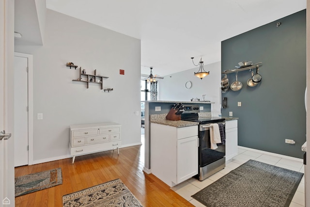 kitchen with stainless steel electric range oven, ceiling fan, white cabinetry, light wood-type flooring, and light stone counters