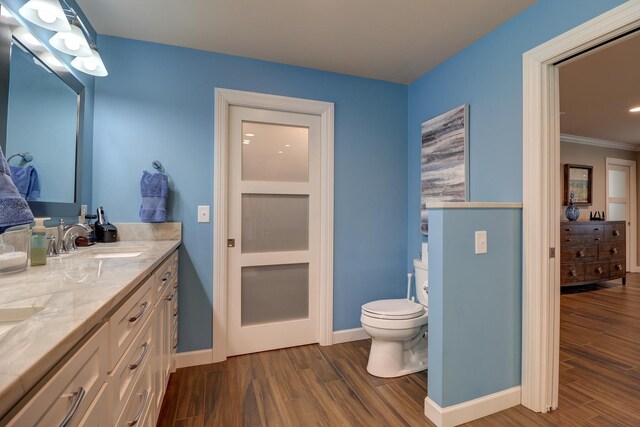 bathroom with wood finished floors, baseboards, toilet, double vanity, and ornamental molding