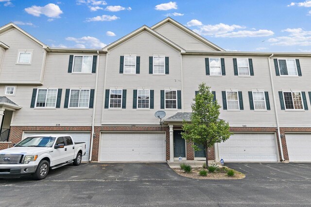 townhome / multi-family property with brick siding, an attached garage, and driveway