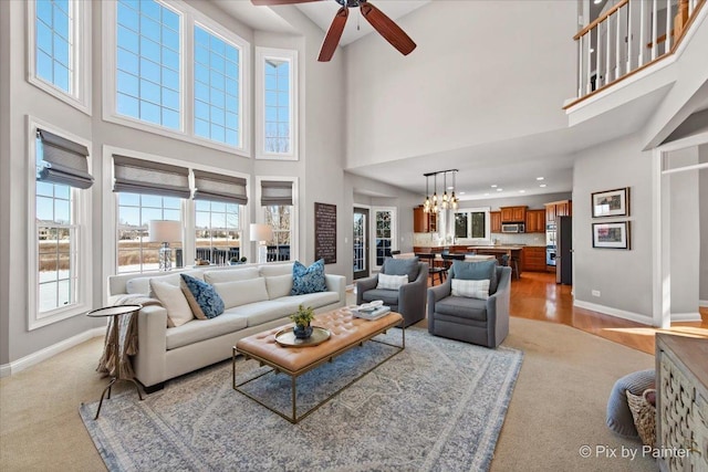 living area with a towering ceiling, baseboards, a ceiling fan, a chandelier, and light colored carpet