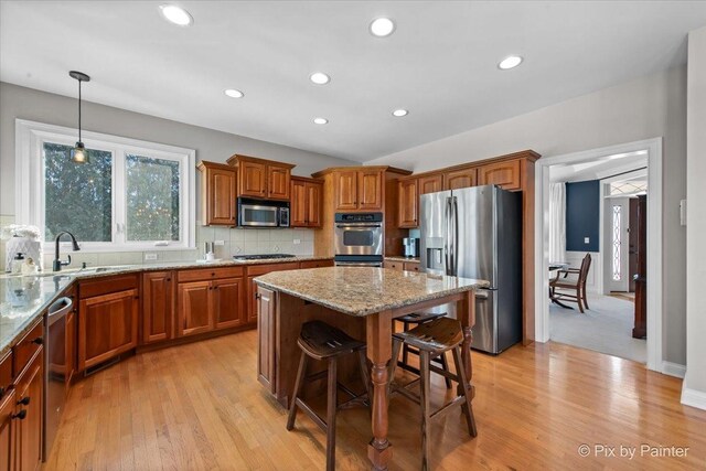 kitchen featuring stainless steel appliances, brown cabinetry, a center island, a breakfast bar, and a sink