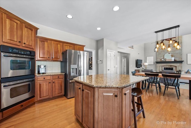 kitchen with stainless steel appliances, a breakfast bar area, light wood finished floors, light stone counters, and recessed lighting