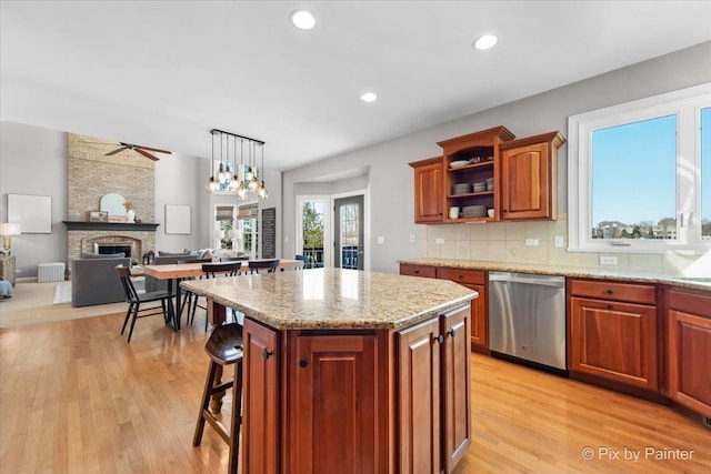 kitchen featuring stainless steel dishwasher, light wood finished floors, a kitchen island, light stone countertops, and tasteful backsplash