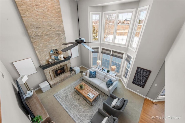 living area with a ceiling fan, a brick fireplace, baseboards, wood finished floors, and a high ceiling