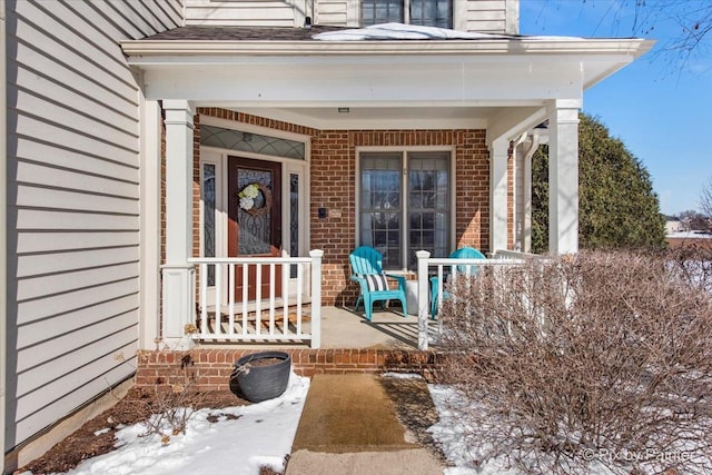 snow covered property entrance featuring covered porch and brick siding
