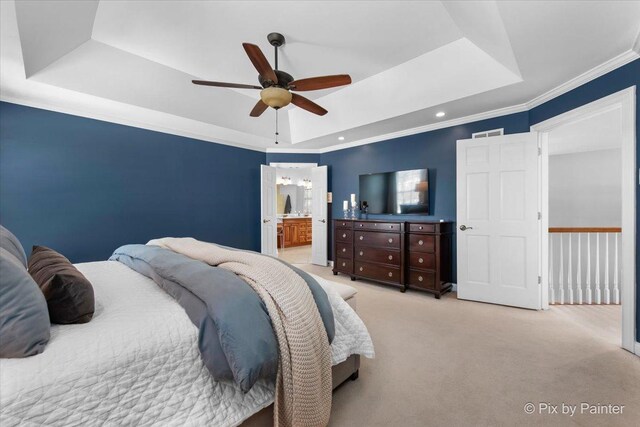 carpeted bedroom featuring a tray ceiling, ornamental molding, ensuite bathroom, and a ceiling fan