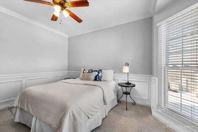 bedroom with carpet floors, ornamental molding, wainscoting, a ceiling fan, and a decorative wall