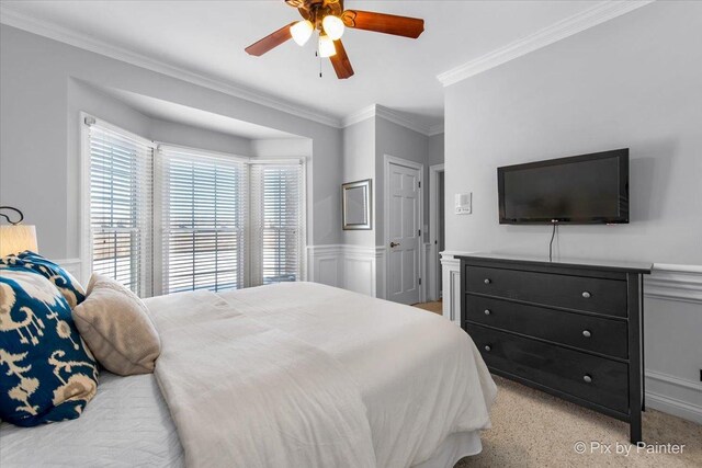 bedroom featuring crown molding, a wainscoted wall, a ceiling fan, and light carpet