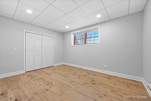 unfurnished bedroom with a paneled ceiling, baseboards, light wood finished floors, a closet, and a baseboard radiator