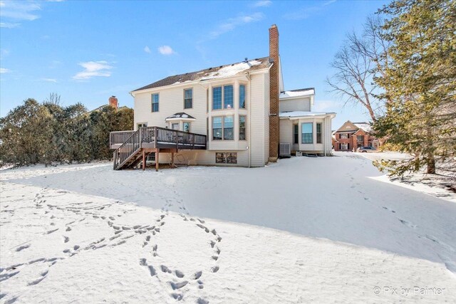 snow covered house featuring stairs, a deck, a chimney, and central AC unit