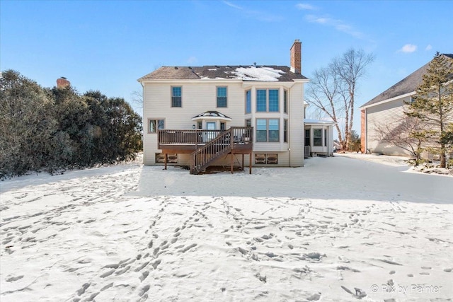 snow covered rear of property featuring a chimney, a wooden deck, and stairway