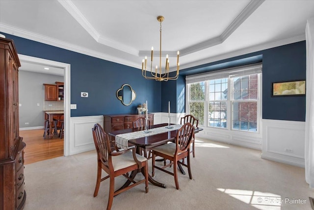 dining space featuring a chandelier, light carpet, wainscoting, a tray ceiling, and ornamental molding