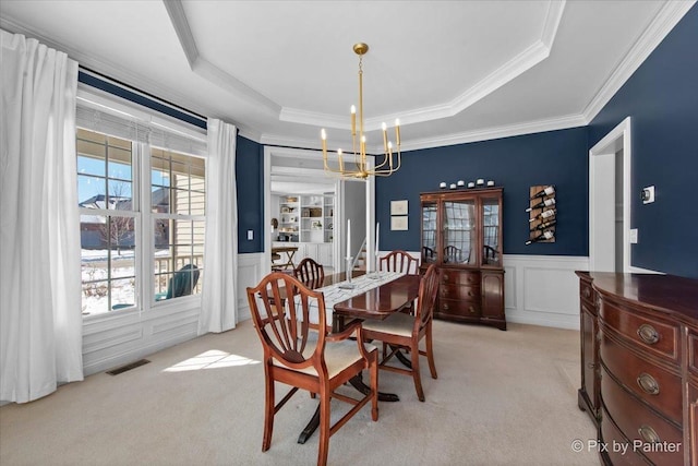 dining room with light colored carpet, a chandelier, a wainscoted wall, a tray ceiling, and plenty of natural light