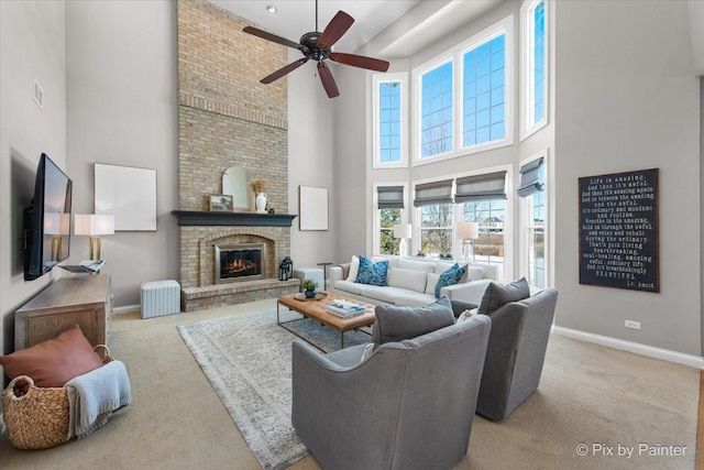 carpeted living room with a towering ceiling, a ceiling fan, baseboards, and a brick fireplace