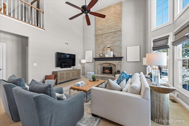 living room featuring a towering ceiling, ceiling fan, carpet, baseboards, and a brick fireplace