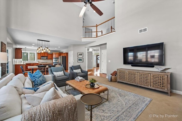 living room featuring light colored carpet, a ceiling fan, baseboards, and a high ceiling