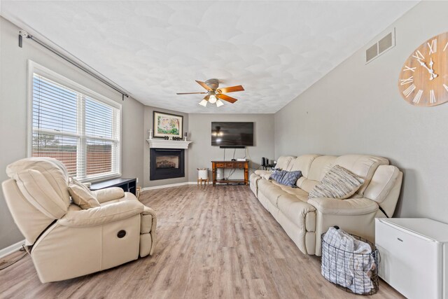 living area featuring a ceiling fan, light wood-style floors, a fireplace, and baseboards