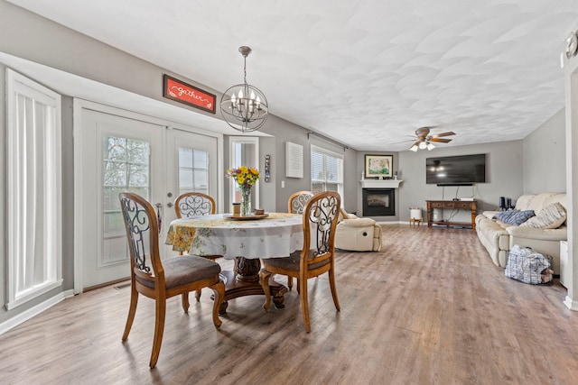 dining space with light wood-type flooring, ceiling fan, a glass covered fireplace, and baseboards