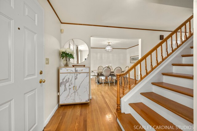 foyer entrance featuring crown molding, stairs, wood finished floors, baseboards, and a chandelier